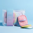Ein transparenter Beutel mit lavendelfarbenem Etikett von INAO by essence enthält mehrere pastellfarbene Swipe Tribe Reusable Makeup Remover Pads. Drei Pads liegen außen auf einer hellblauen Oberfläche und sorgen für saubere Haut.